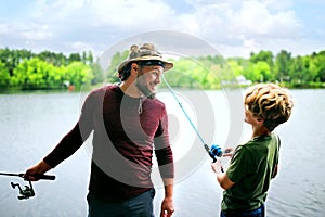 Father and his young son are on a dock on a small lake fishing while on summer vacation.