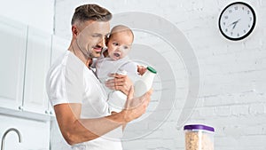 father holding baby daughter and showing bottle