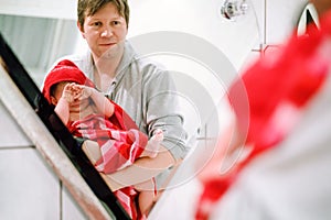 Father holding cute little toddler girl wrapped in towel after taking bath. Happy healthy baby child with wet hairs