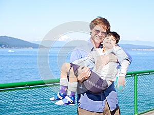 Father holding disabled son in arms on deck of ferry boat.