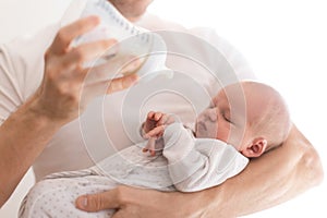 Father holding and feeding his newborn son with milk bottle at home.