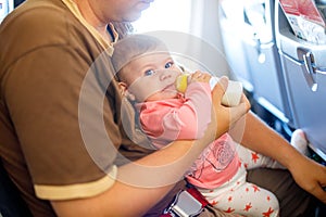 Father holding his baby daughter during flight on airplane going on vacations