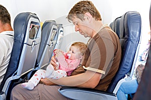 Father holding his baby daughter during flight on airplane going on vacations