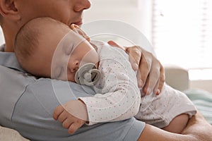 Father holding his cute sleeping baby with pacifier at home, closeup