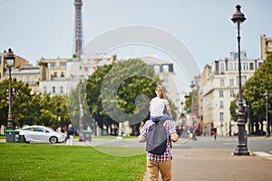 Father holding his daughter on shoulders and walking on a street of Paris