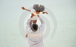 Father holding his daughter up high against sky. african american dady hug girl with sea background