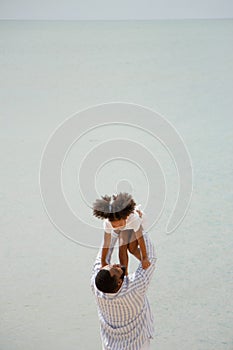 Father holding his daughter up high against sky. african american dady hug girl with sea background