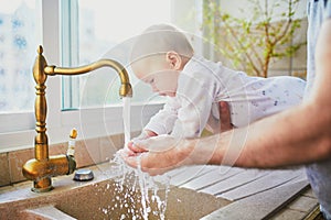 Father holding his little baby girl helping her to wash hands