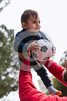 Father holding his little son up in the air with a soccer ball while playing together outdoors in the park.