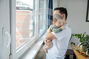 Father holding his newborn son, looking through window