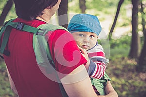 Father holding his son in baby carrier walking in the park