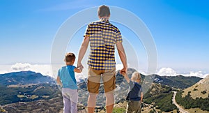 Father holding his sons in arms and looking at the mountains, rear view