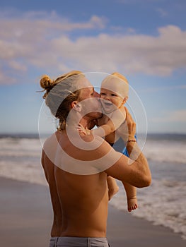 Father holding, kissing his infant baby boy son high in the air on sandy beach. Family travel and summer vacations concept. Family