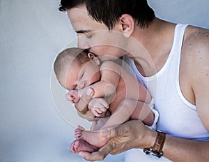 Father holding newborn baby kissing his head eyes closed