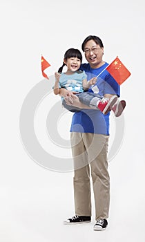 Father holding smiling and happy daughter in his arms, waving Chinese flags, studio shot