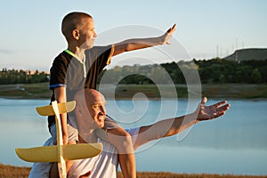 Father holding son on shoulders at sunset with airplane in hand