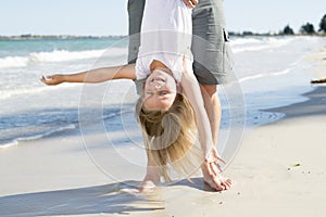 Father holding sweet young and lovely blond small daughter by her feet playing having fun on the beach in dad and little girl love