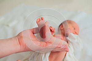 Father holds the feet of newborn. Small legs of child in the hands of parent close-up. Newborn baby care concept