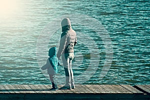 The father holds his child by the hand on the pontoon of a lake.
