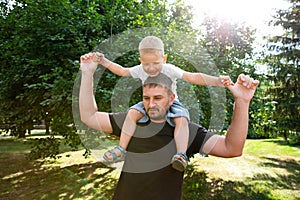 Father holds his son on his back like an airplane in park outdoor. Father plaing with son. Kindred love. Affection. Trusting photo