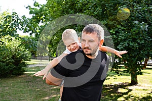 Father holds his son on his back like an airplane in park outdoor. Father plaing with son. Kindred love. Affection. Trusting photo