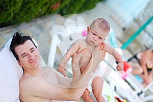 The father holds the little son in his arms and they rest together after swimming in the pool