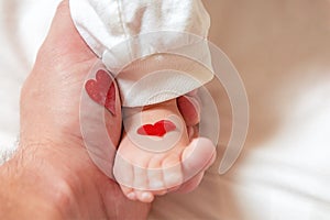 Father holds a small leg of a newborn baby. hearts for parents d