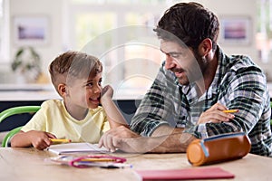 Father At Home In Kitchen Helping Son With Homework