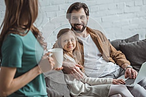 father hugging daughter and looking at mother with cup