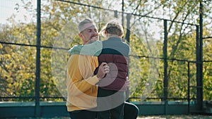Father hugs his son after basketball practice and they go away, on a sunny day