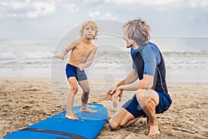 Father or instructor teaching his 4 year old son how to surf in