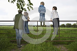 Father With Kids Looking At Lush Landscape By Fence