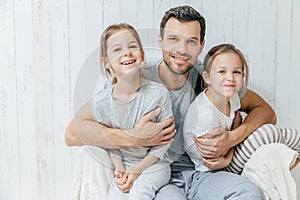 Father and kids. Paternity concept. Handsome unshaven affectionate dad embraces his two pretty dauhters, going to have walk