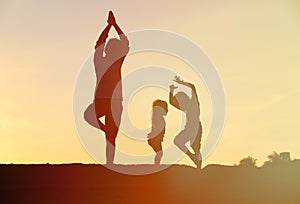 Father with kids silhouettes doing yoga at sunset