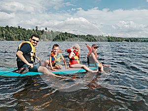 Father with kids swimming on paddle surf board on lake river. Dad with children doing sport summer water activity outdoors.