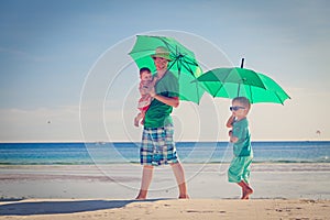Father and kids with umbrellas on beach vacation