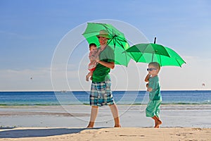 Father and kids with umbrellas on beach vacation