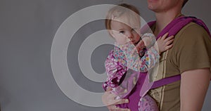 Father kisses the child, gray background space for text. Carrying baby in sling
