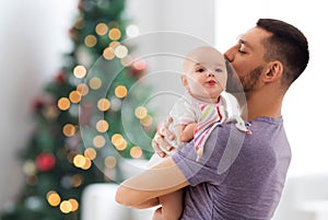 Father kissing baby daughter over christmas tree