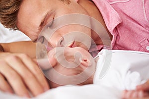 Father Kissing Baby Girl As They Lie In Bed Together