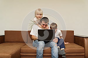 Father with laptop sitting on couch with his two sons. kids took dad to rest