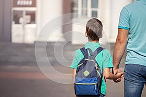 Father leads a little child school boy go hand in hand. Parent and son with backpack behind the back