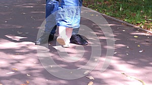 Father learning baby girl to walk, first steps in park, legs closeup.