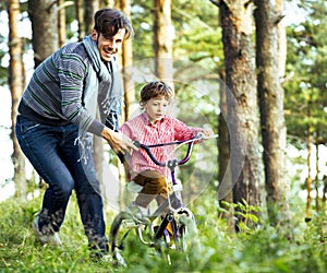 Father learning his son to ride on bicycle outside, real happy family, lifestyle people concept