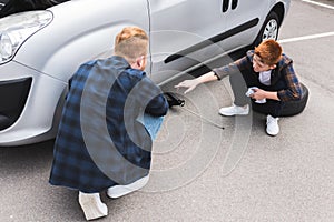 father lifting car with floor jack for changing tire son pointing