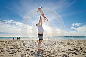 Father lifting daughter, having fun on the beach. A smiling young man playing with his cute little girl on vacation. Fun