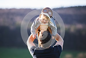 A father lifting his toddler son in the air outside in spring nature.