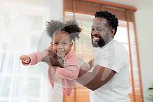 Father lifting toddler daughter in the air while enjoying a day at living room with smile. Refreshment spending time together.