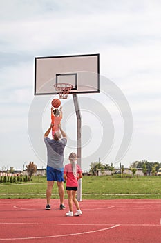 The father lifts his daughter high up to throw the ball into the basketball hoop
