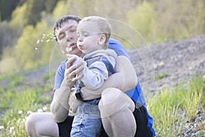 Father and little child are blowing into a white dandelion flower. Close-up